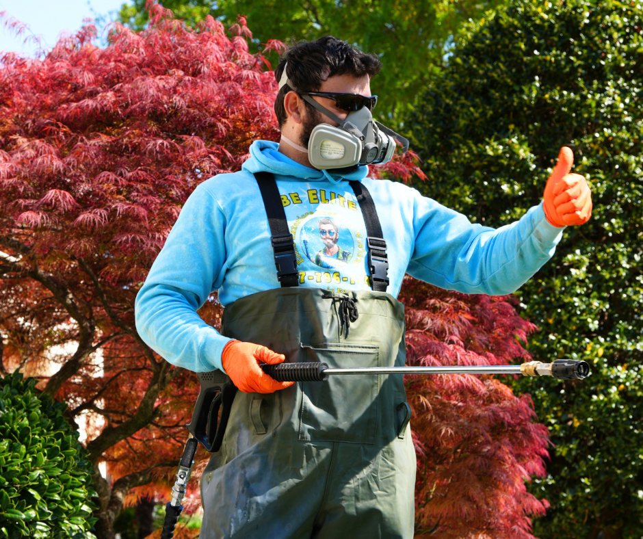Professional pressure washing technician wearing protective gear and holding a pressure washing wand while giving a thumbs-up in a residential yard.