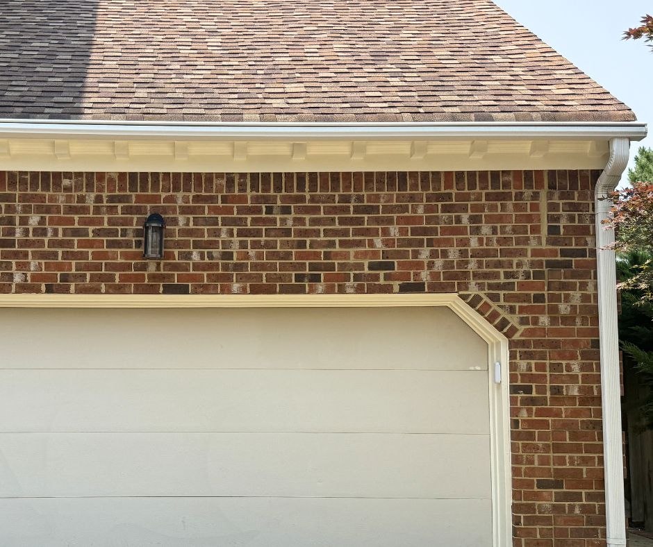 Clean white gutters and downspouts installed along a brick home's roofline, showcasing a well-maintained exterior drainage system.