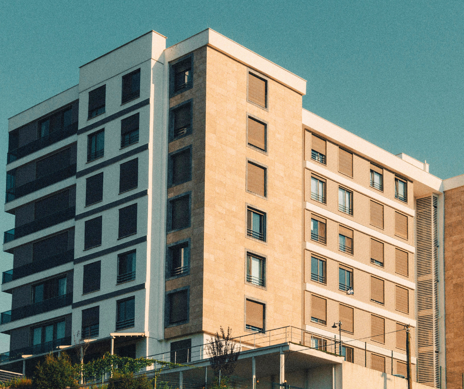 Modern multi-story residential apartment building with brick and white exterior walls, large windows, balconies, and rooftop structures under a clear blue sky.